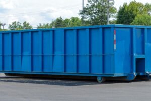 a blue, residential dumpster sits on asphalt