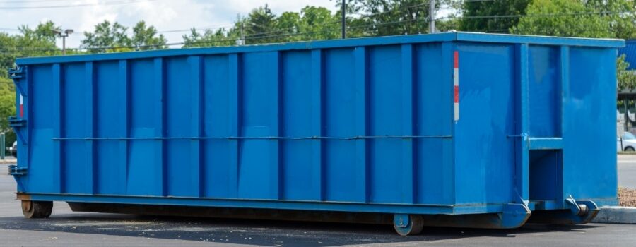 a blue, residential dumpster sits on asphalt
