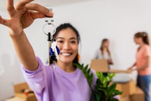 asian woman holding a potted plant smiles and holds up home keys
