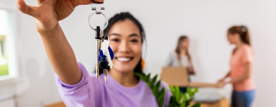 asian woman holding a potted plant smiles and holds up home keys