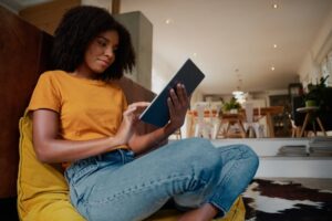 a black woman sits cross legged in a chair reading a tablet