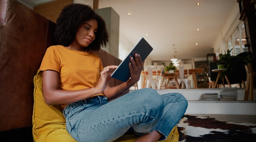a black woman sits cross legged in a chair reading a tablet